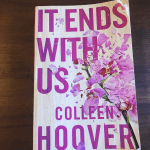 Photo of Colleen Hoover's novel It Ends With Us sitting on a dark brown desk.